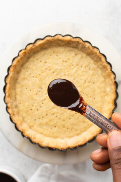 Overhead view of a baked tart shell in a a tart tin, blind baked tart pastry crust on white marble countertop, process of making tart