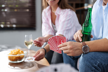Friends playing cards at table indoors, selective focus