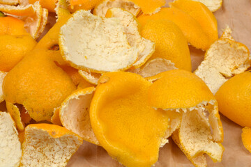 A close-up overhead shot features large, roughly peeled pieces of bright yellow mandarin peel scattered across a crumpled, brown craft paper background, highlighting the texture and color contrast