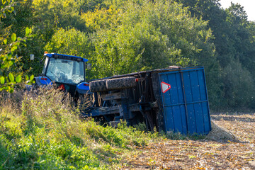 Overturned farm trailer with spilled corn beside tractor in field after agricultural accident during harvest season © Adam