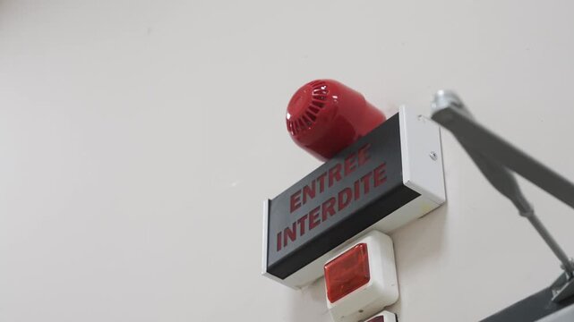 A close-up on a wall-mounted warning system for a restricted area. A sign reads "ENTREE INTERDITE" (Do Not Enter) and is fitted with an alarm siren and flashing light.
