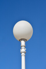 A vertical, low-angle shot features a white spherical street lamp with a decorative metal base, sharply contrasted against a clear, bright blue sky