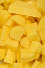 A  close-up shot fills the frame with a bright yellow pile of freshly peeled and uniformly cubed raw potatoes, ready for cooking