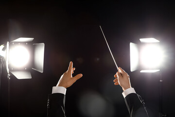 Hands of male conductor with baton on black background