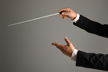 Hands of male conductor with baton on grey background
