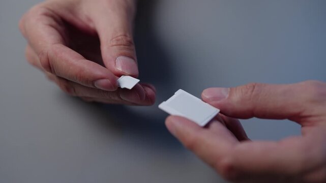 Close-up of male hands holding micro SD card and SD card adapter, inserting small memory card into larger adapter for data storage and electronic device compatibility. Shooting in slow motion.