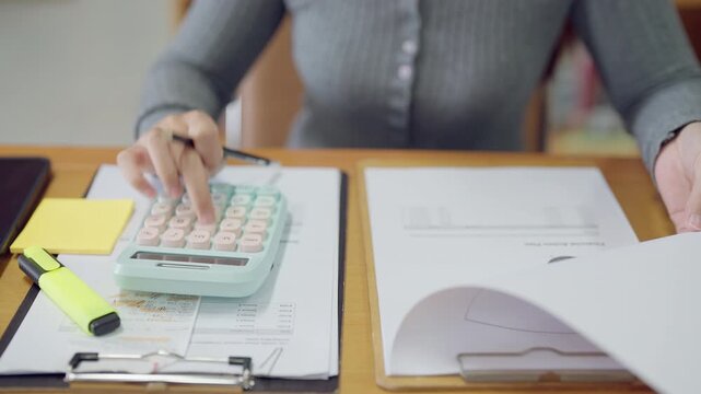Close-up of woman calculating financial budget using calculator at office desk. Accounting, finance, and data management theme.