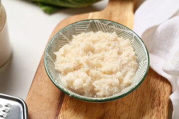 Wooden cutting board and bowl with horseradish sauce on white background, closeup