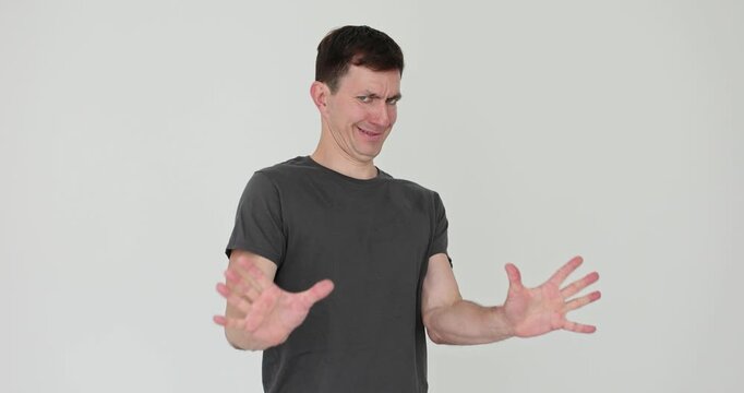 Man pulls torso back showing disgust with tight face. Person raises hands forward and rejects approach signalling strong No with gesture in studio
