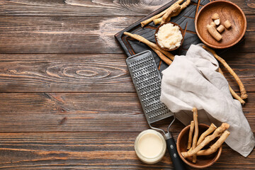 Composition with grater, horseradish roots, sauce in bowl and jar on brown wooden background
