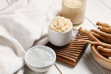 Cutting board, horseradish roots and sauce in bowl on white wooden background, closeup