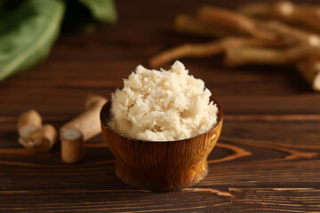Bowl with horseradish sauce on brown wooden background, closeup
