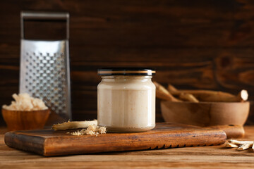 Board and glass jar with horseradish sauce on brown wooden background