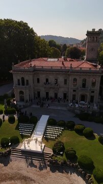 Aerial drone view of historic Villa Erba on Lake Como with bell tower, floral arch, and semicircle rows of chairs set for luxury destination wedding overlooking the scenic lake and mountains