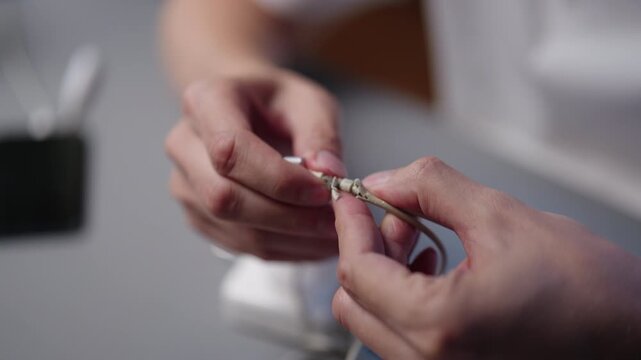 Hands holding critically frayed and broken charging cable, exposed copper wires indicating severe damage and potential electrical hazard from extended wear and tear , close-up, slow motion.