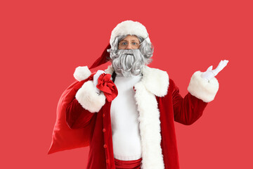 Santa Claus with bag full of gifts showing something on red background