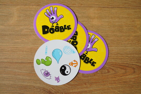 Close-up of Dobble game cards, featuring various symbols and the Dobble logo on a wooden surface