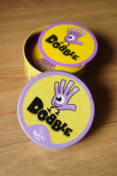 Close-up of the popular Dobble card game, also known as Spot It!, with its distinct purple and yellow packaging and playful hand logo, showcasing the fun and engaging family game on a wooden surface