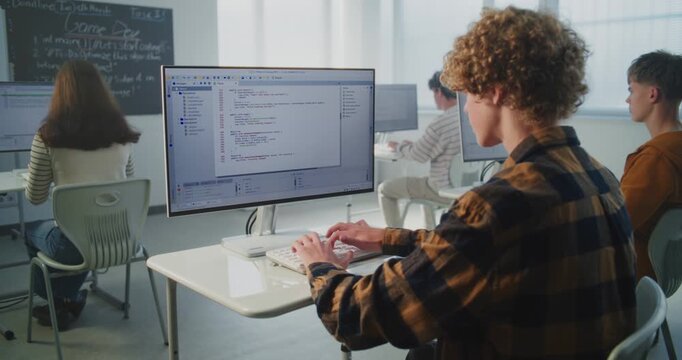 Focused Student Types Computer Code Quickly on Keyboard. Male Student Sits at Desk in Classroom, Intently Writing Program Code. Concept of Modern Education, and Future Technology Skills. Static Shot.