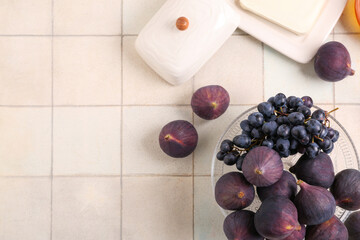 Bowl with fresh ripe figs and grape on beige tile background, closeup