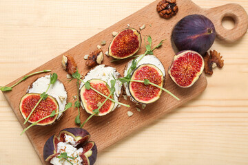 Cutting board, sandwiches with fresh ripe fig and arugula on beige wooden background, closeup
