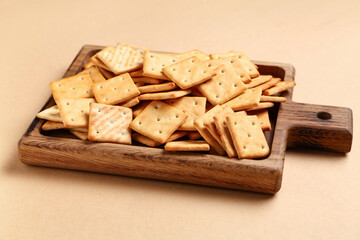 Wooden board with tasty crackers on beige background, closeup