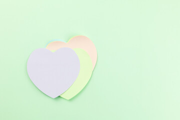A stack of pastel heart-shaped sticky notes, purple, light green, and light pink hues, on green background. Top view, ideal for themes of love, communication, reminders, or creative projects.