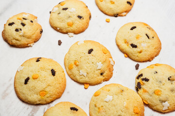 Halloween cookies with spooky funfetti confetti candy sprinkles shaped like ghosts, bats and pumpkins on white background, freshly baked golden sugar and butter biscuits