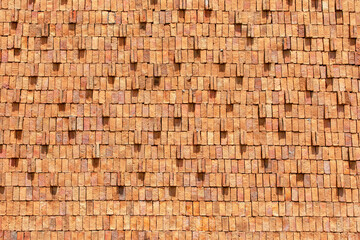 Close-up texture of stacked orange clay bricks arranged in a uniform pattern. The surface reveals natural tones, rough textures, and geometric repetition