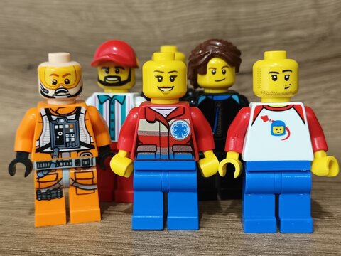 A collection of five different LEGO minifigures, featuring a paramedic, a pilot, and other characters, displayed in a group on a wooden background