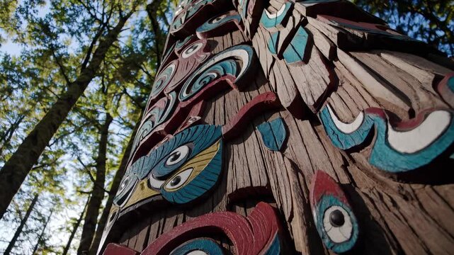 Low-angle video shot of a colorful totem pole in a sunlit forest, highlighting intricate carvings against a backdrop of towering trees.