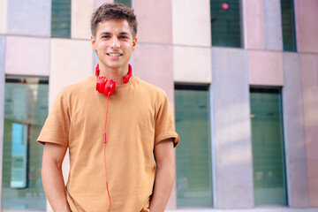 Young man wearing a brown t-shirt and red headphones around his neck, looking directly at the...