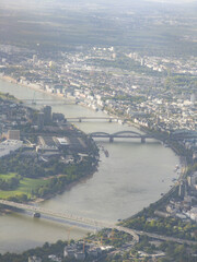Aerial view of the Rhine River winding through Cologne city center, with bridges and green spaces under a cloudy sky