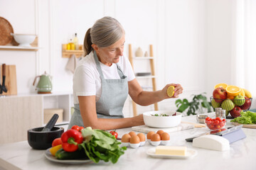 Senior woman cooking salad at white marble table in kitchen