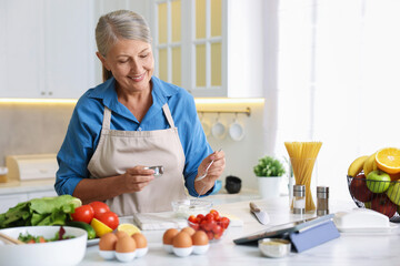 Senior woman cooking at white marble table in kitchen