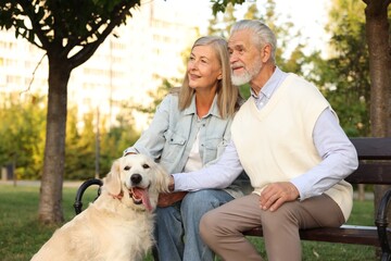 Happy senior couple with adorable Golden Retriever dog on bench outdoors