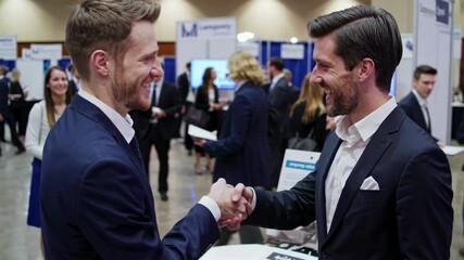 Professional networking event captured in a candid video style, with a side-angle view of two businessmen shaking hands in a busy conference setting. - Powered by Adobe