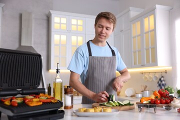 Man cutting zucchini while cooking vegetables on electric grill in kitchen