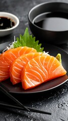Fresh salmon sashimi on a black plate, with soy sauce and perilla garnish