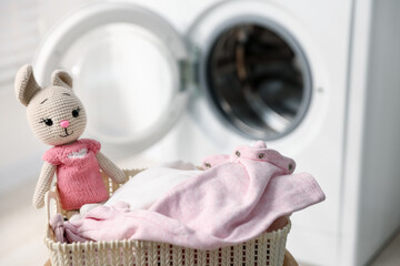 Laundry basket with baby clothes and toy bunny near washing machine, selective focus