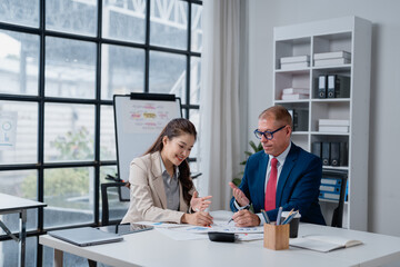 Two business professionals, an experienced male mentor and a young female mentee, are collaborating in an office setting, analyzing financial documents and discussing strategies together