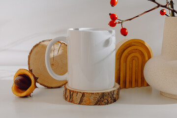 Ceramic mockup mug with rose hips in vase and autumn decorations with aesthetic shadows. White mug on wooden coaster for autumn design