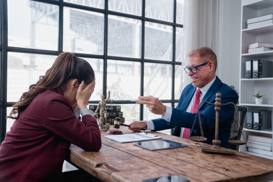 Female client sitting at a desk, covering her face and looking stressed while a male lawyer, gesturing with his hand and holding a gavel, is scolding her in an emotional legal consultation