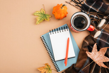 Autumn flat lay with coffee cup, notebooks, pen, pumpkin, leaves and plaid scarf on beige background. Cozy seasonal workspace concept. Top view, mockup