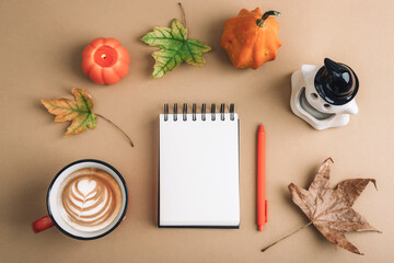 Cozy autumn flat lay with latte art coffee, notebook, pen, pumpkin candle and fall leaves on beige background. Warm seasonal concept, top view, mockup
