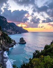Fototapeta premium Coastal sunrise over a secluded bay. Dramatic clouds and warm colors paint the sky above a rocky coastline