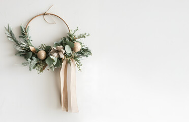 Minimal Christmas wreath crafted from eucalyptus and pine branches, decorated with simple paper ornaments and linen ribbon, hanging on clean white wall, Scandinavian style, airy neutral design