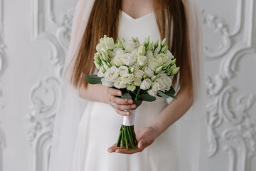 Elegant bride in a white satin gown holding a round bridal bouquet of white eustoma (lisianthus)...