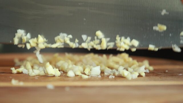Fresh garlic cloves being chopped and diced on a rustic wooden cutting board with a sharp knife, showcasing essential food preparation technique