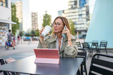 Businesswoman talking on phone drinking coffee at outdoor cafe